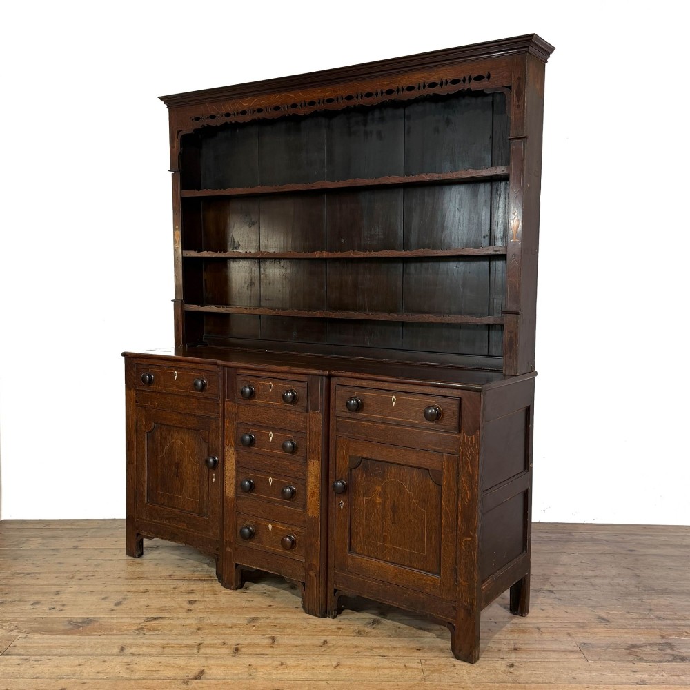 An antique 19th-century dark oak North Wales dresser featuring an open three-shelf plate rack with a pierced fretwork frieze above a base with two cupboards and four central drawers. View III