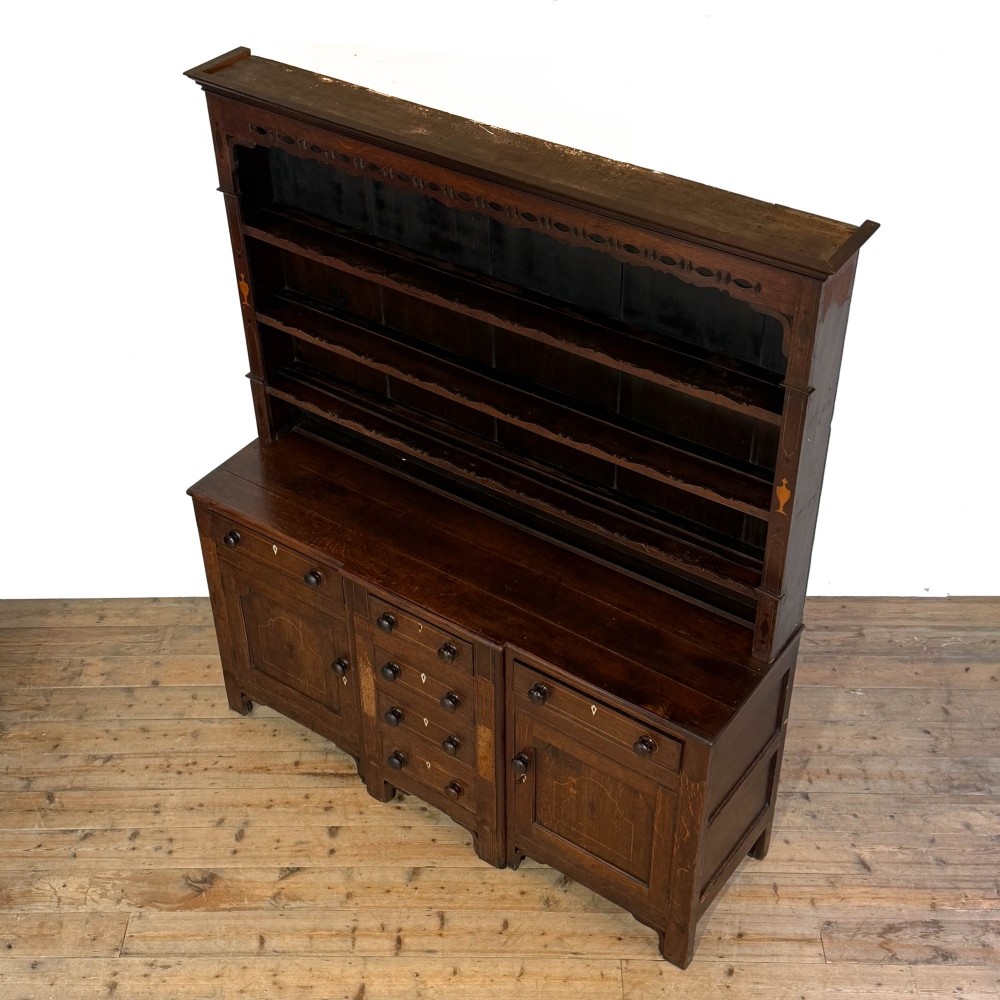 An antique 19th-century dark oak North Wales dresser featuring an open three-shelf plate rack with a pierced fretwork frieze above a base with two cupboards and four central drawers. View IV