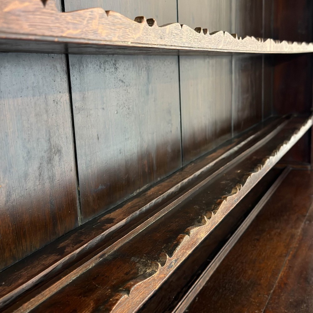 An antique 19th-century dark oak North Wales dresser featuring an open three-shelf plate rack with a pierced fretwork frieze above a base with two cupboards and four central drawers. View X