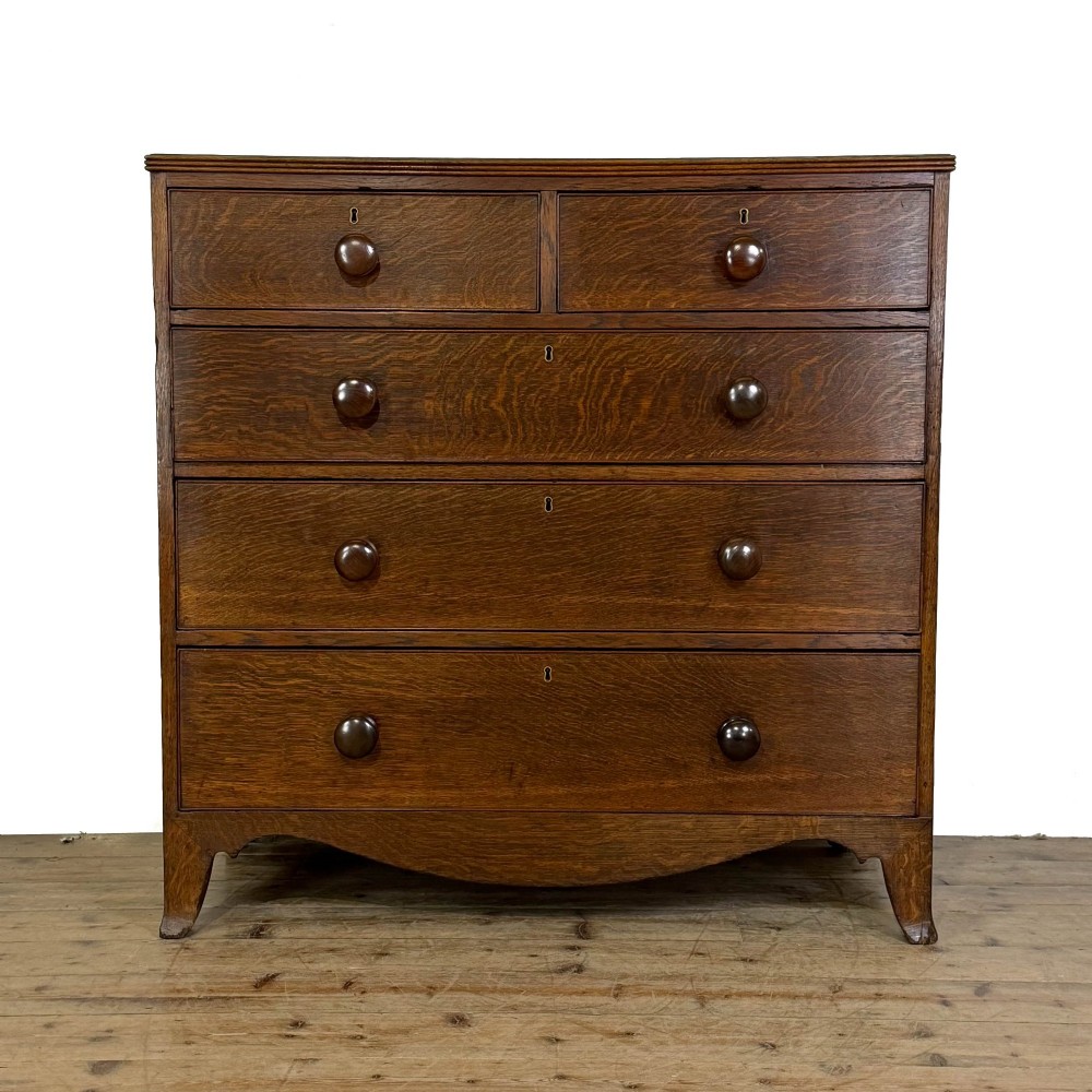 An antique Georgian oak chest of drawers featuring two short drawers over three long drawers with turned wooden knobs and a shaped apron.