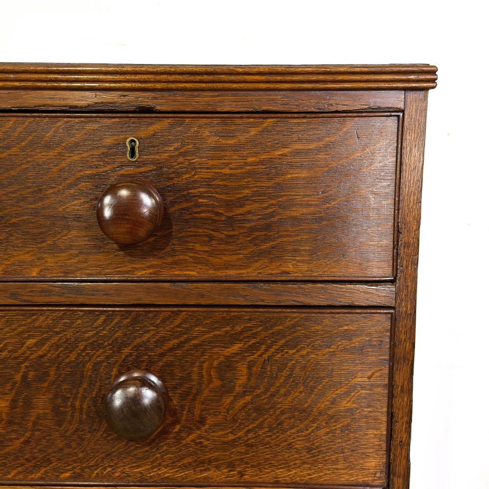 An antique Georgian oak chest of drawers featuring two short drawers over three long drawers with turned wooden knobs and a shaped apron. View III