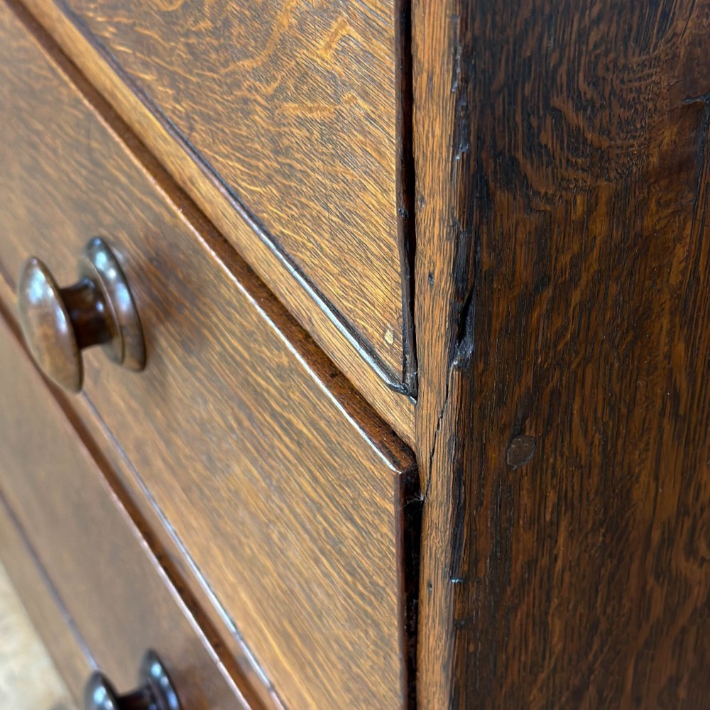 An antique Georgian oak chest of drawers featuring two short drawers over three long drawers with turned wooden knobs and a shaped apron. View IV
