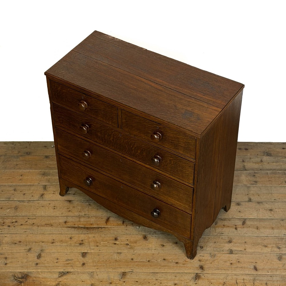 An antique Georgian oak chest of drawers featuring two short drawers over three long drawers with turned wooden knobs and a shaped apron. View VI
