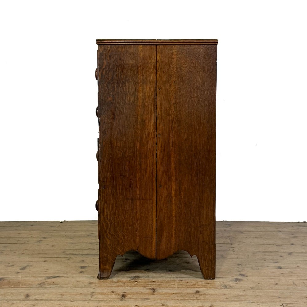 An antique Georgian oak chest of drawers featuring two short drawers over three long drawers with turned wooden knobs and a shaped apron. View VIII
