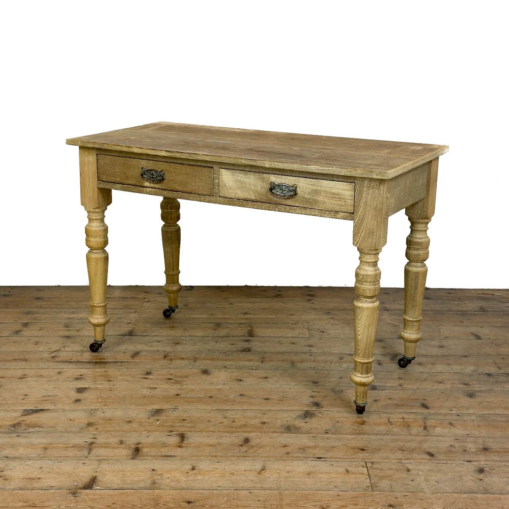 An antique stripped pine side table featuring two drawers with metal drop handles and four turned legs on castors. View II