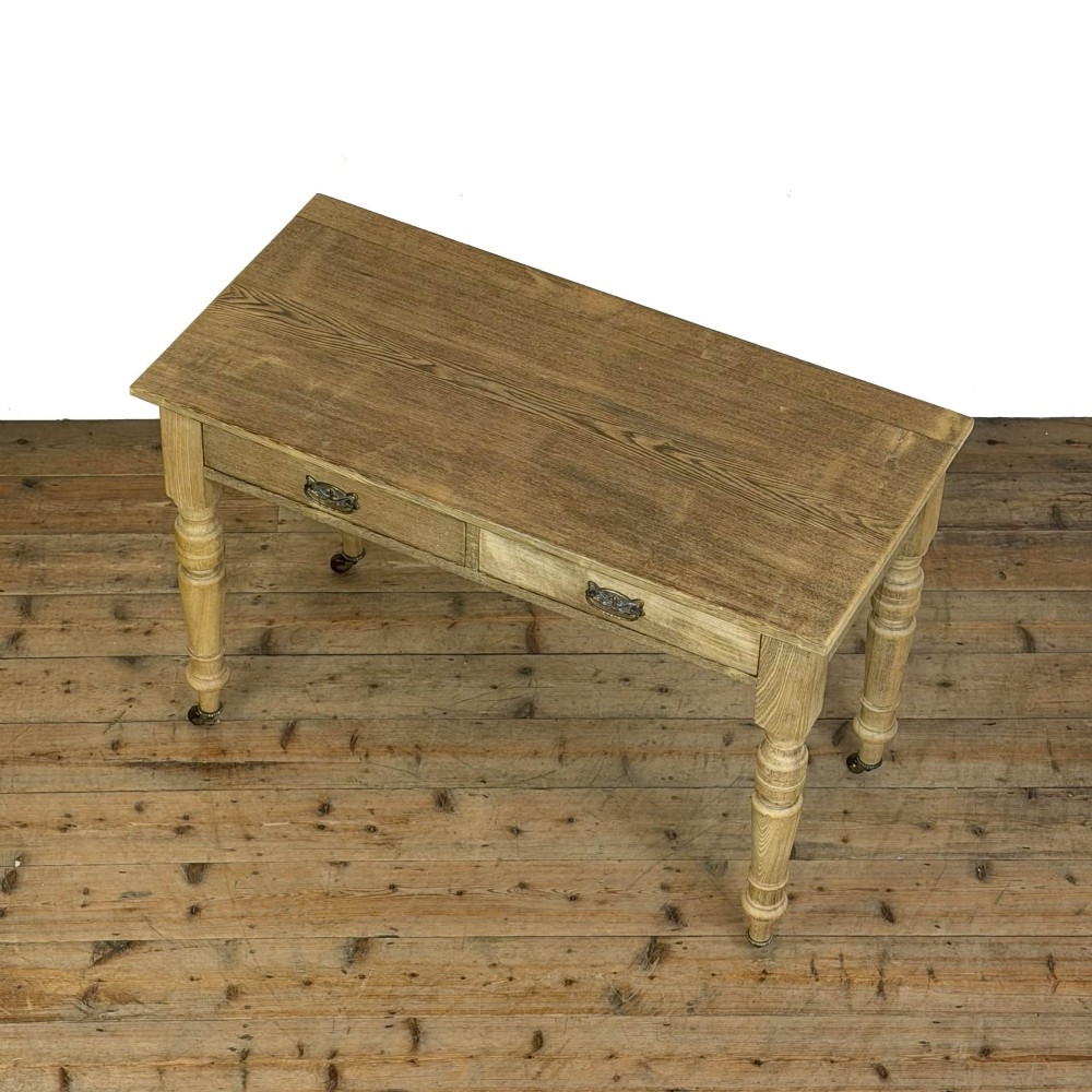 An antique stripped pine side table featuring two drawers with metal drop handles and four turned legs on castors. View III