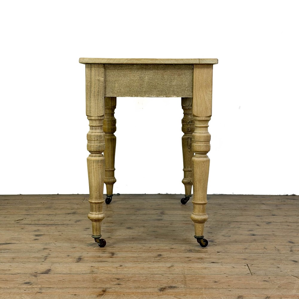 An antique stripped pine side table featuring two drawers with metal drop handles and four turned legs on castors. View IV