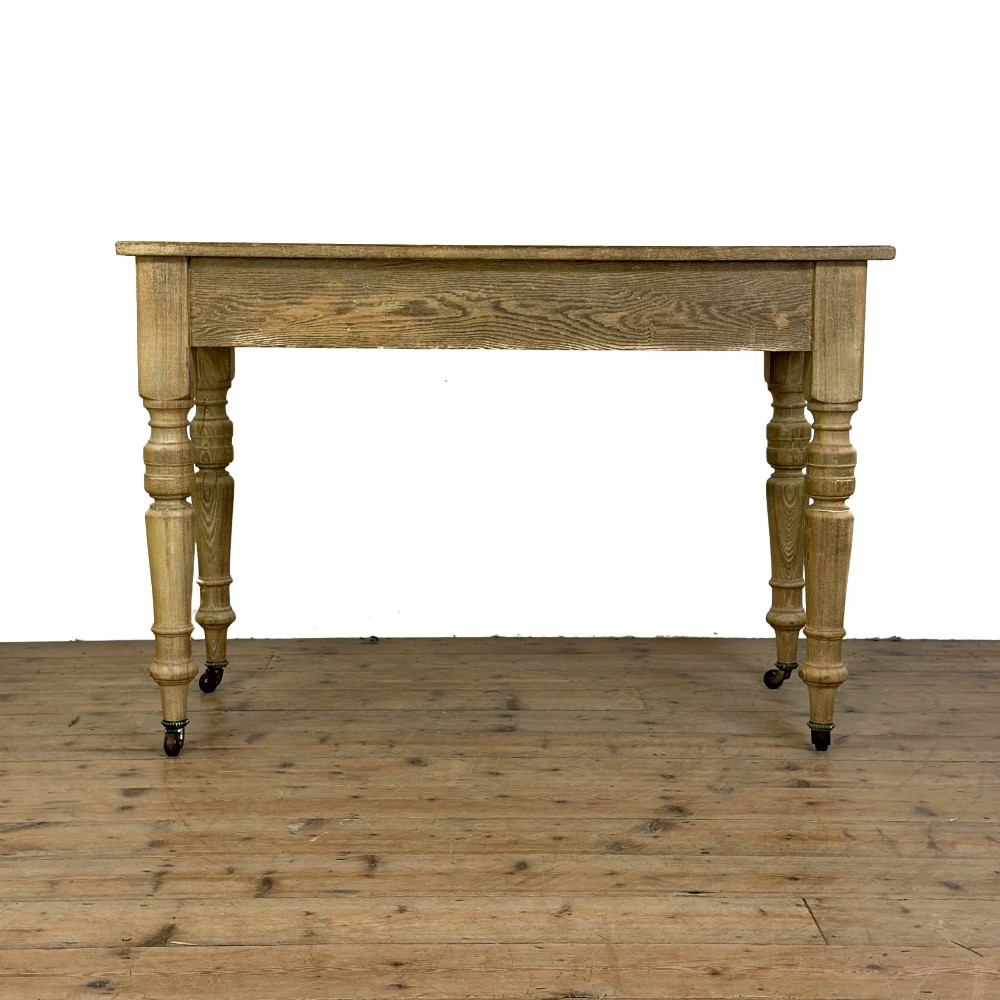 An antique stripped pine side table featuring two drawers with metal drop handles and four turned legs on castors. View VI