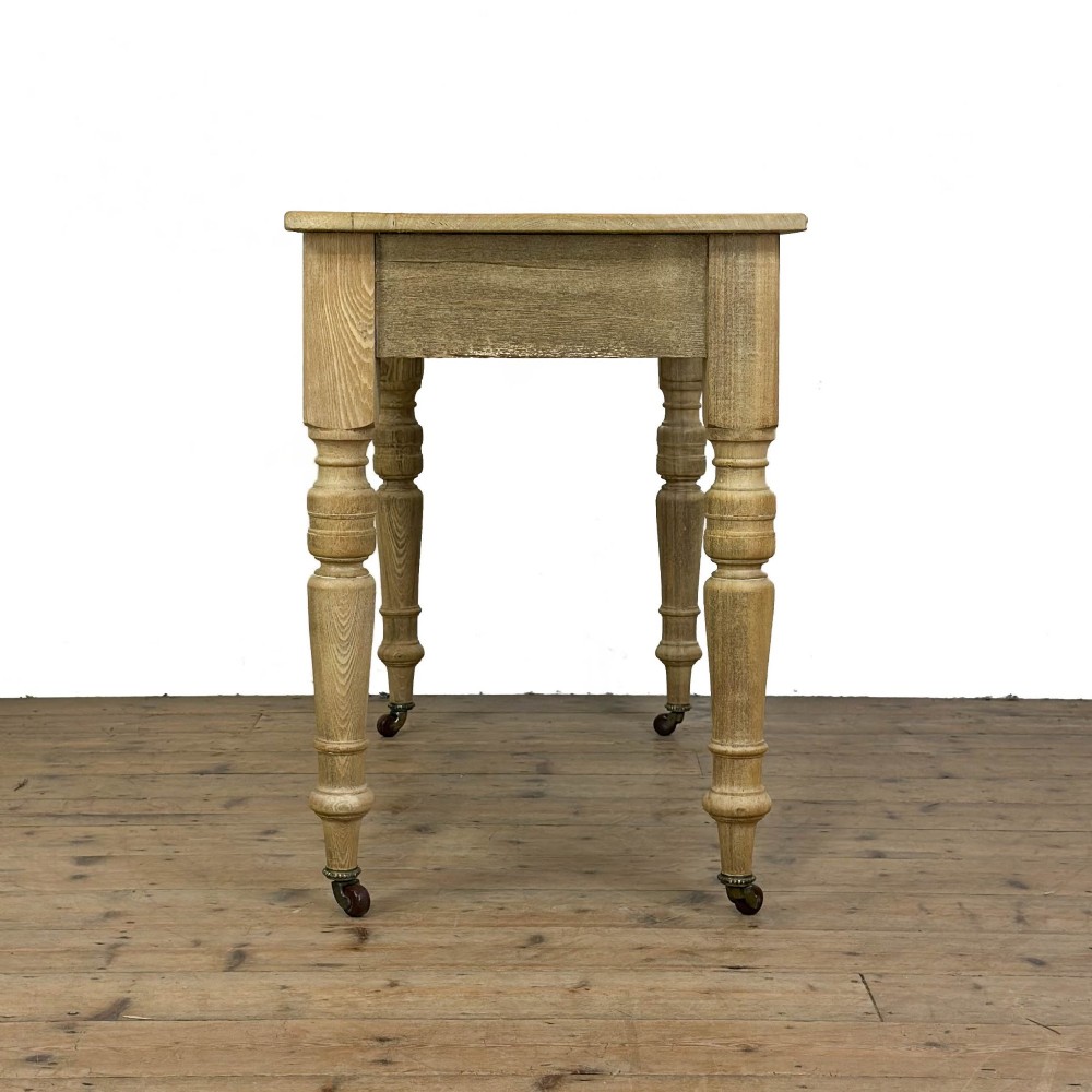 An antique stripped pine side table featuring two drawers with metal drop handles and four turned legs on castors. View VIII