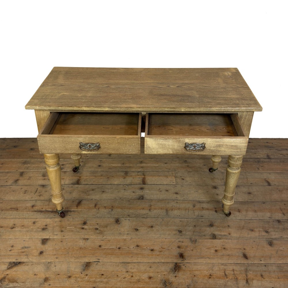 An antique stripped pine side table featuring two drawers with metal drop handles and four turned legs on castors. View IX