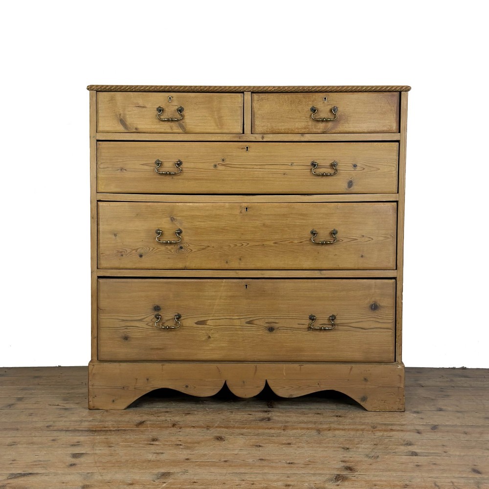 A Victorian stripped pine chest of drawers featuring a two-over-three drawer configuration, brass drop handles, and a shaped apron.