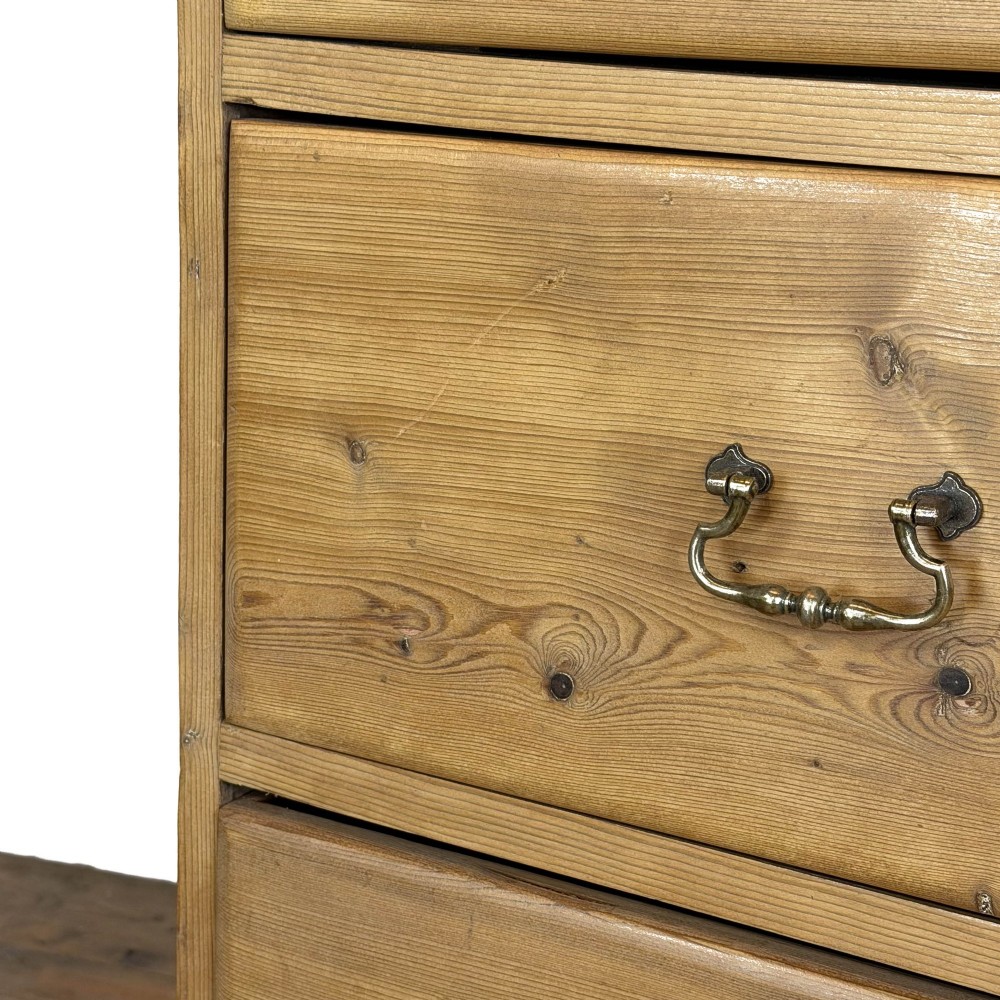 A Victorian stripped pine chest of drawers featuring a two-over-three drawer configuration, brass drop handles, and a shaped apron. View III