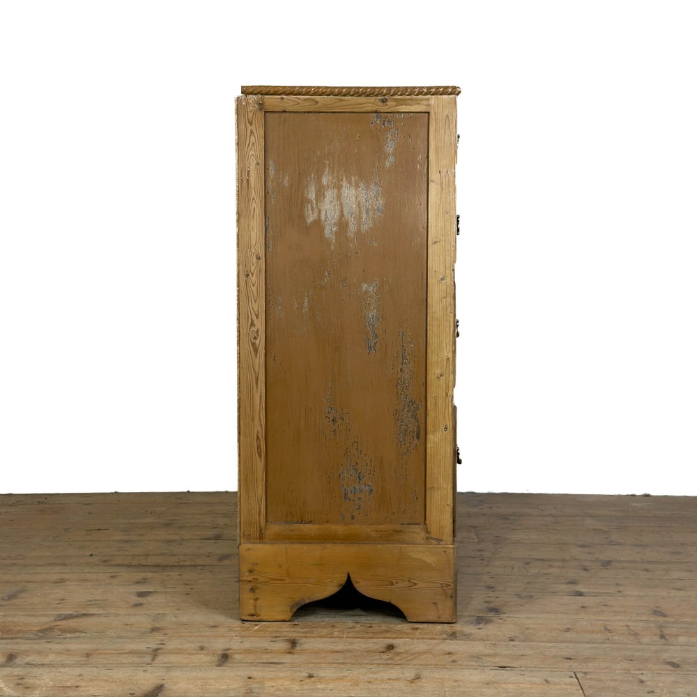 A Victorian stripped pine chest of drawers featuring a two-over-three drawer configuration, brass drop handles, and a shaped apron. View V