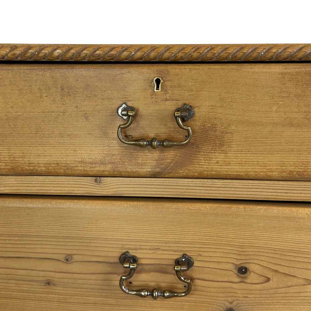 A Victorian stripped pine chest of drawers featuring a two-over-three drawer configuration, brass drop handles, and a shaped apron. View VI