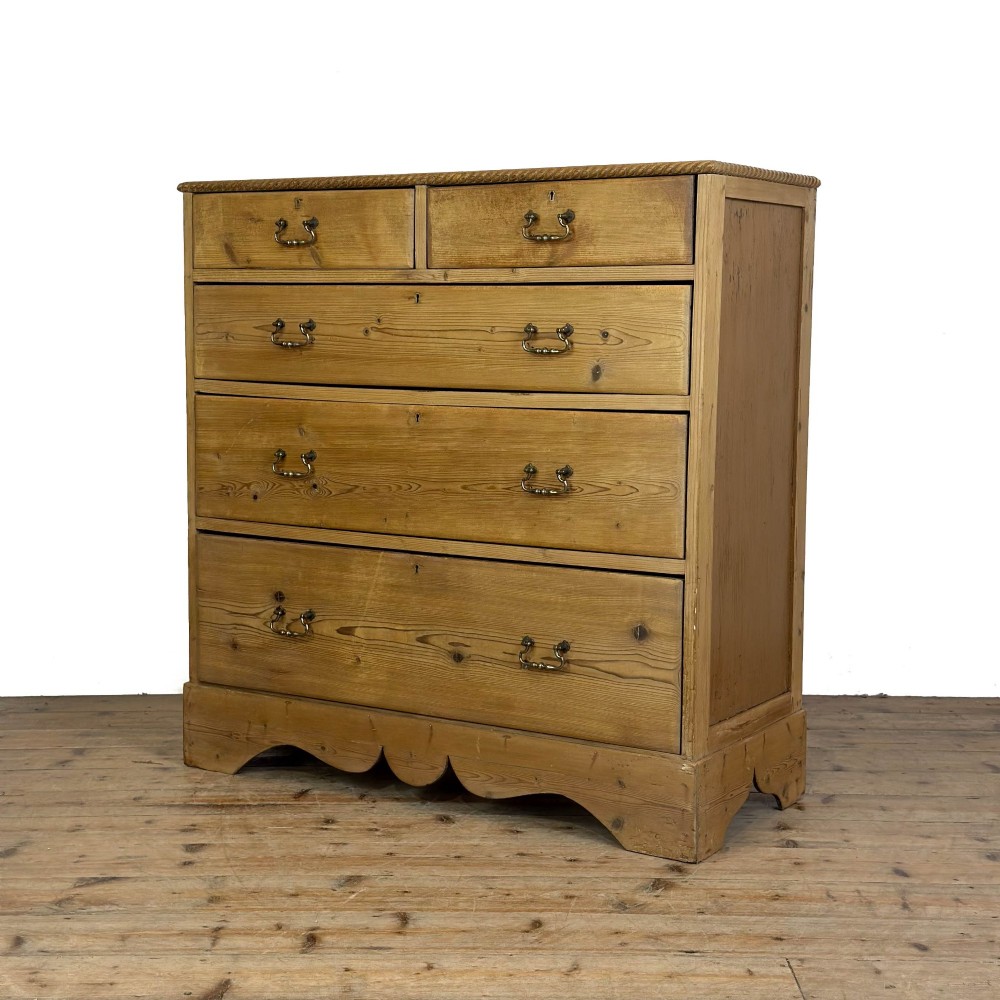 A Victorian stripped pine chest of drawers featuring a two-over-three drawer configuration, brass drop handles, and a shaped apron. View VII