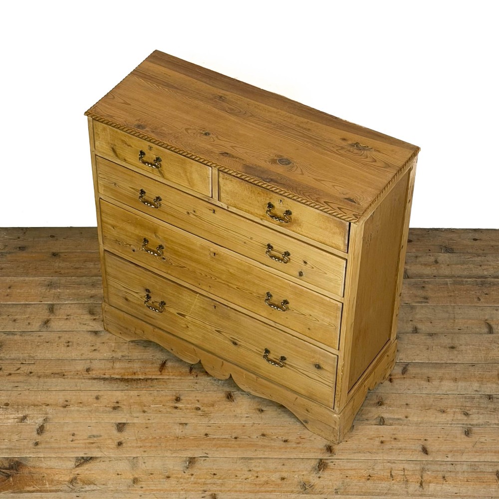 A Victorian stripped pine chest of drawers featuring a two-over-three drawer configuration, brass drop handles, and a shaped apron. View VIII