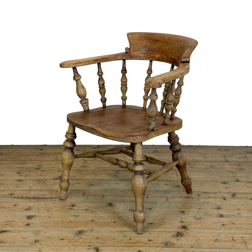 An antique wooden smokers bow armchair with turned spindles, a curved horseshoe armrest, and turned legs.