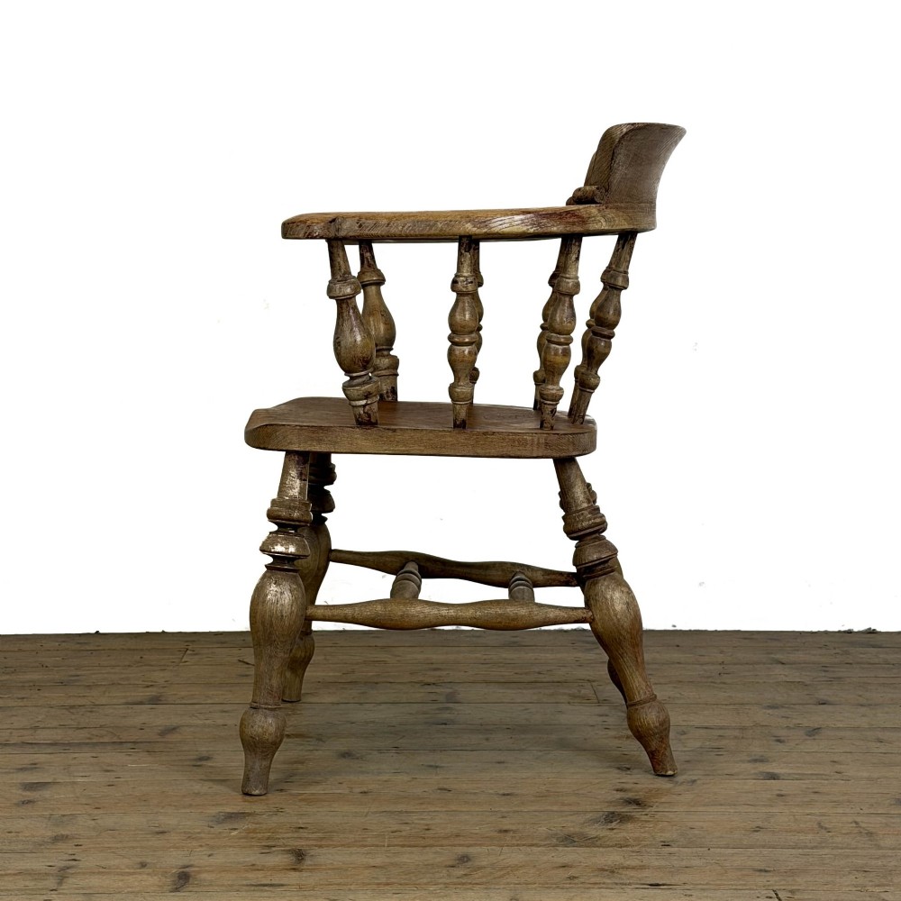 An antique wooden smokers bow armchair with turned spindles, a curved horseshoe armrest, and turned legs. View II