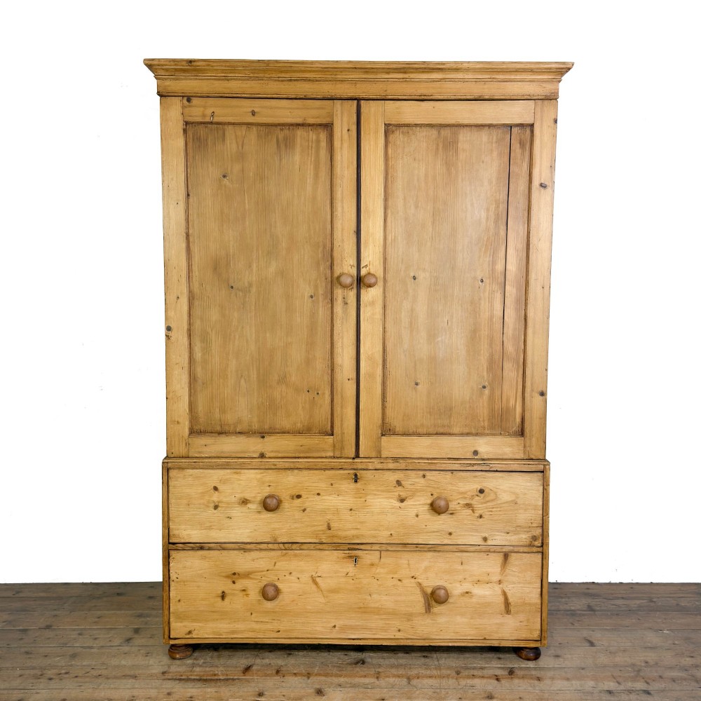 A 19th-century pine linen press featuring a moulded cornice, two upper panelled doors, two wide lower drawers with wooden knob handles, resting on turned bun feet.
