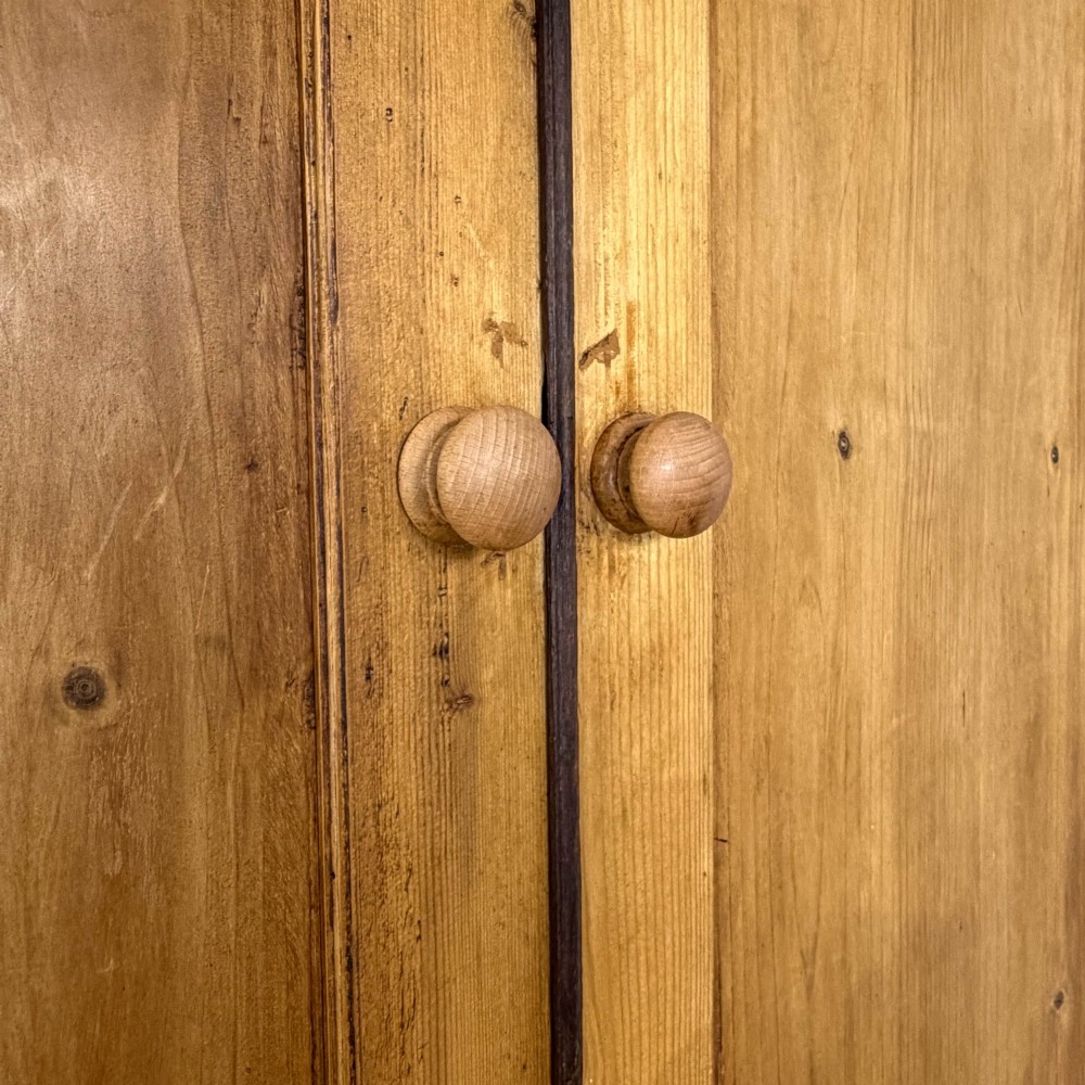 A 19th-century pine linen press featuring a moulded cornice, two upper panelled doors, two wide lower drawers with wooden knob handles, resting on turned bun feet. View VII