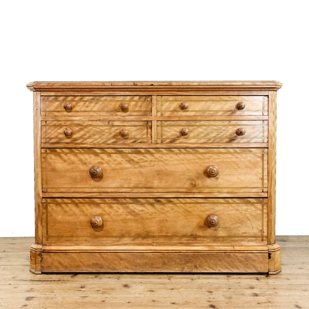A Victorian satinwood chest of drawers with turned wooden handles, subtle geometric inlaid banding, and a broad plinth base.