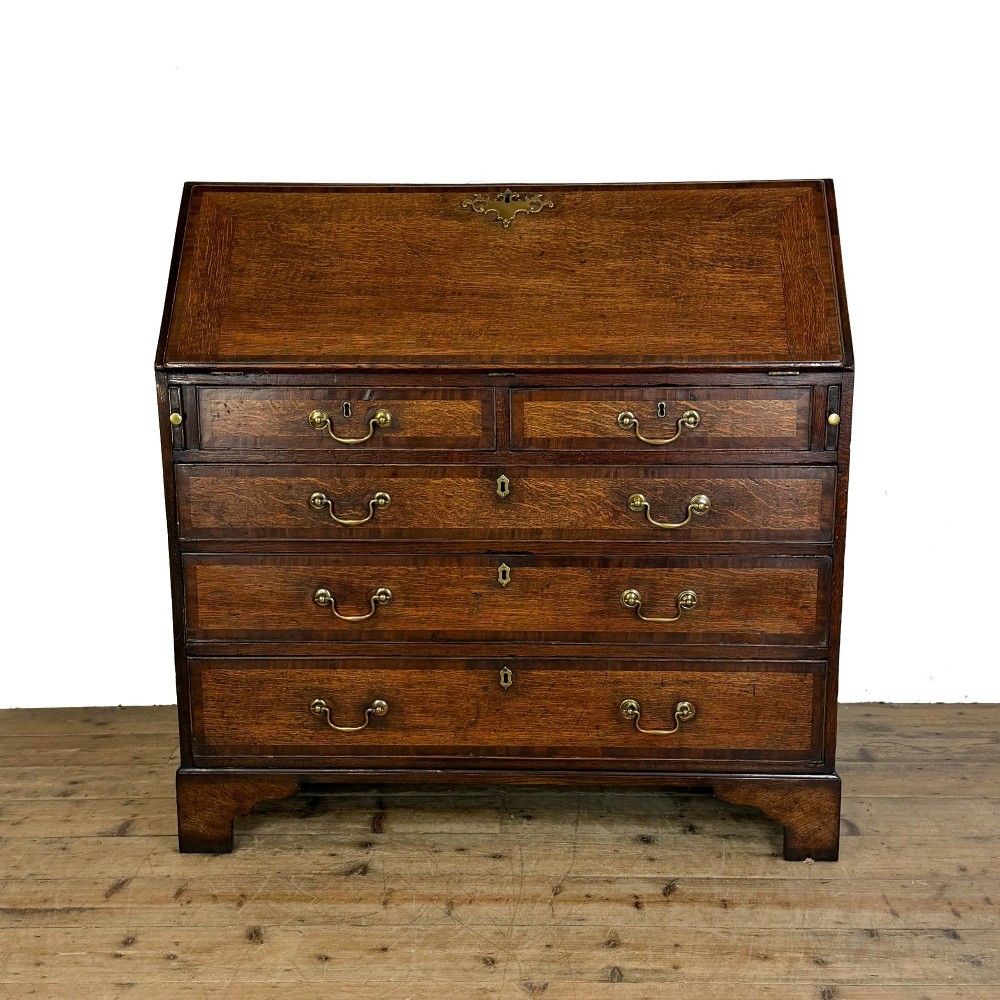 An antique Georgian oak writing bureau featuring a sloping fall-front lid above four drawers with brass swan-neck handles.