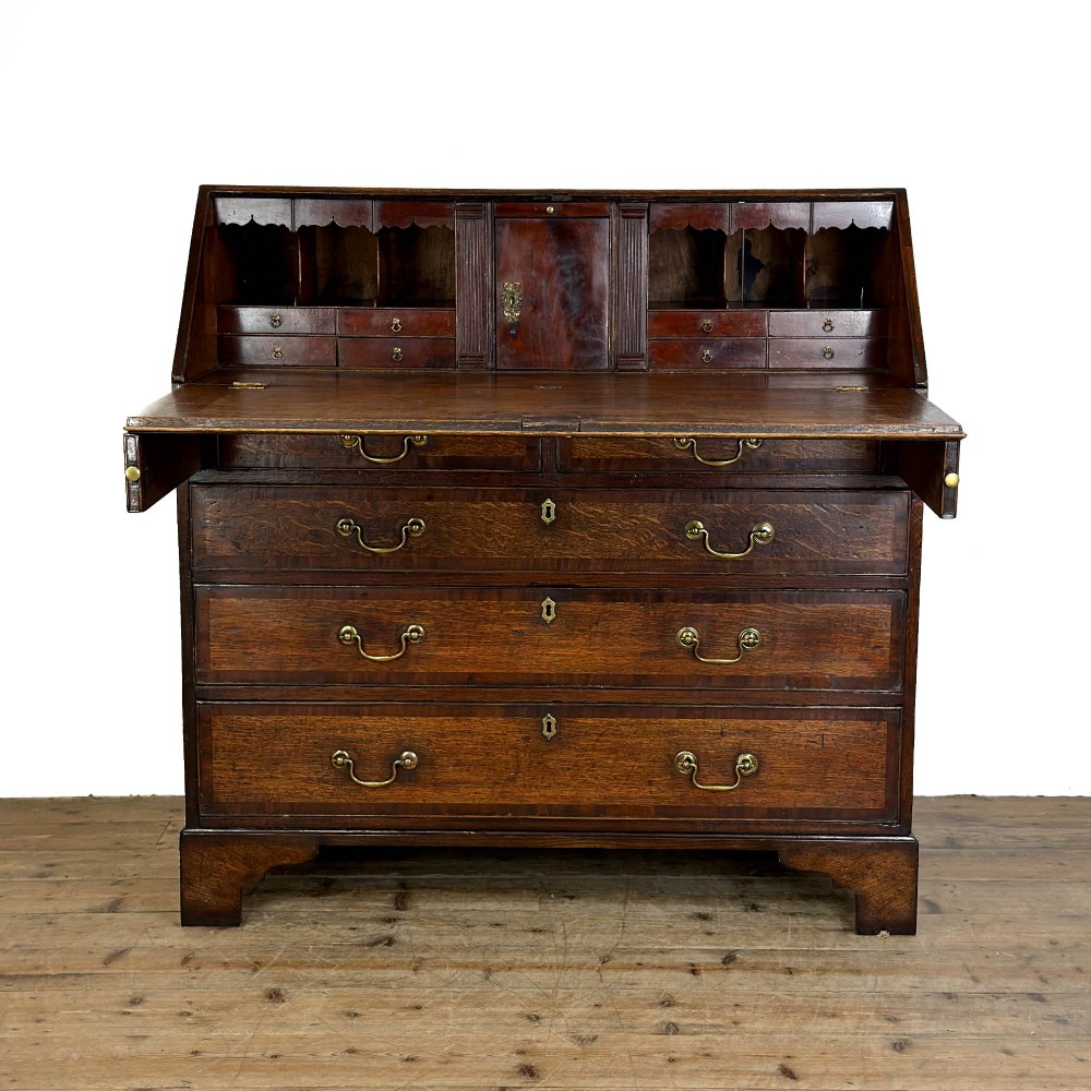 An antique Georgian oak writing bureau featuring a sloping fall-front lid above four drawers with brass swan-neck handles. View II