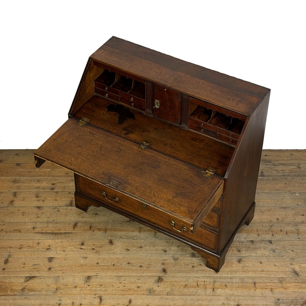 An antique Georgian oak writing bureau featuring a sloping fall-front lid above four drawers with brass swan-neck handles. View V