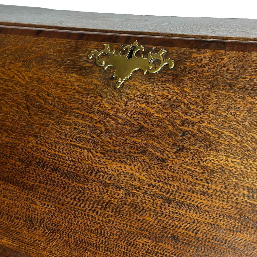 An antique Georgian oak writing bureau featuring a sloping fall-front lid above four drawers with brass swan-neck handles. View VI