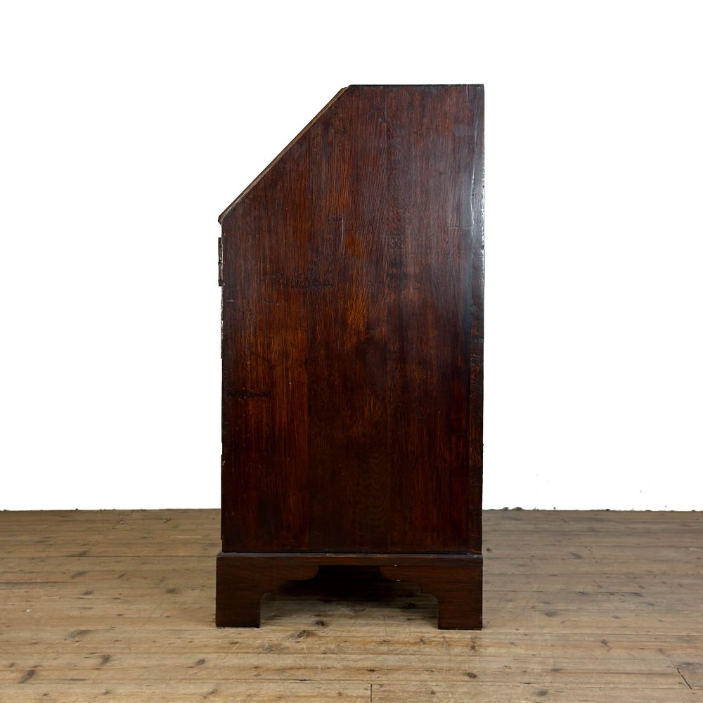 An antique Georgian oak writing bureau featuring a sloping fall-front lid above four drawers with brass swan-neck handles. View VIII