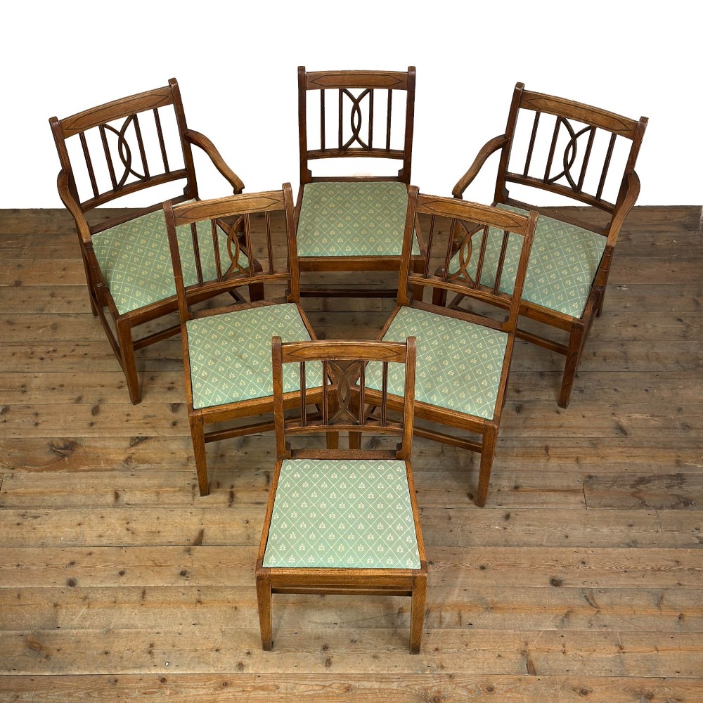 A set of six antique oak dining chairs, including two carvers, featuring geometric inlaid crest rails, decorative back splats, and light green patterned fabric seats. View II