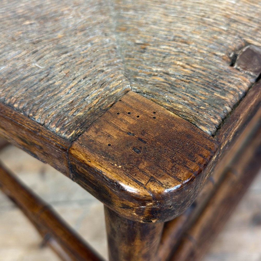 An antique dark brown wooden rocking chair with faux bamboo turnings, a high spindle back, and a woven rush seat. View II