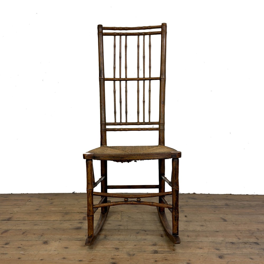 An antique dark brown wooden rocking chair with faux bamboo turnings, a high spindle back, and a woven rush seat. View III