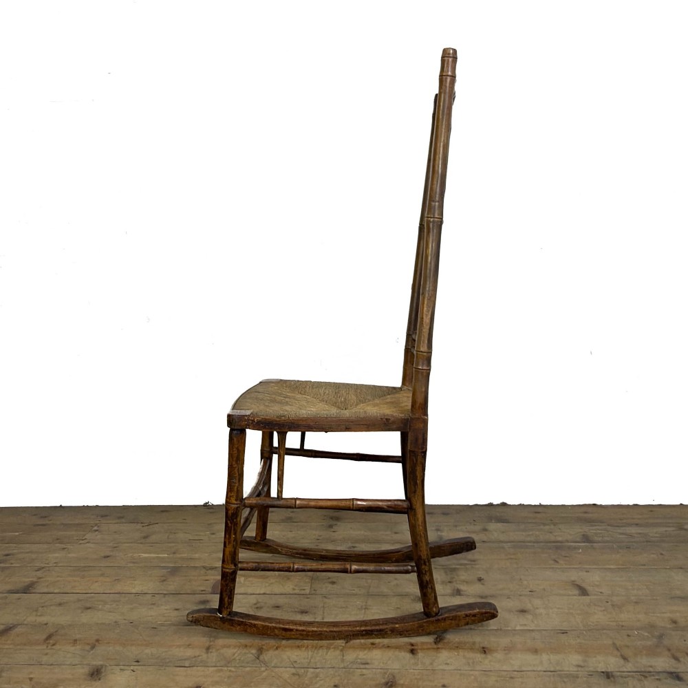 An antique dark brown wooden rocking chair with faux bamboo turnings, a high spindle back, and a woven rush seat. View IV