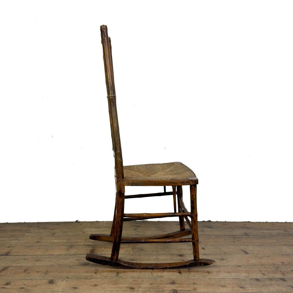 An antique dark brown wooden rocking chair with faux bamboo turnings, a high spindle back, and a woven rush seat. View VI