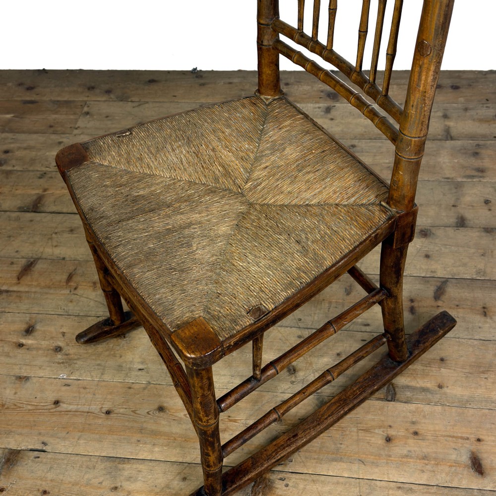 An antique dark brown wooden rocking chair with faux bamboo turnings, a high spindle back, and a woven rush seat. View VII