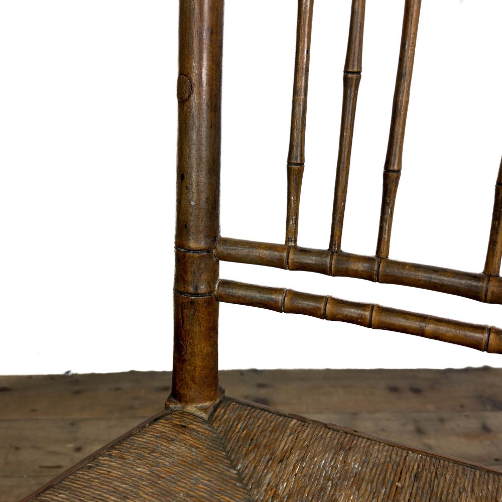 An antique dark brown wooden rocking chair with faux bamboo turnings, a high spindle back, and a woven rush seat. View VIII