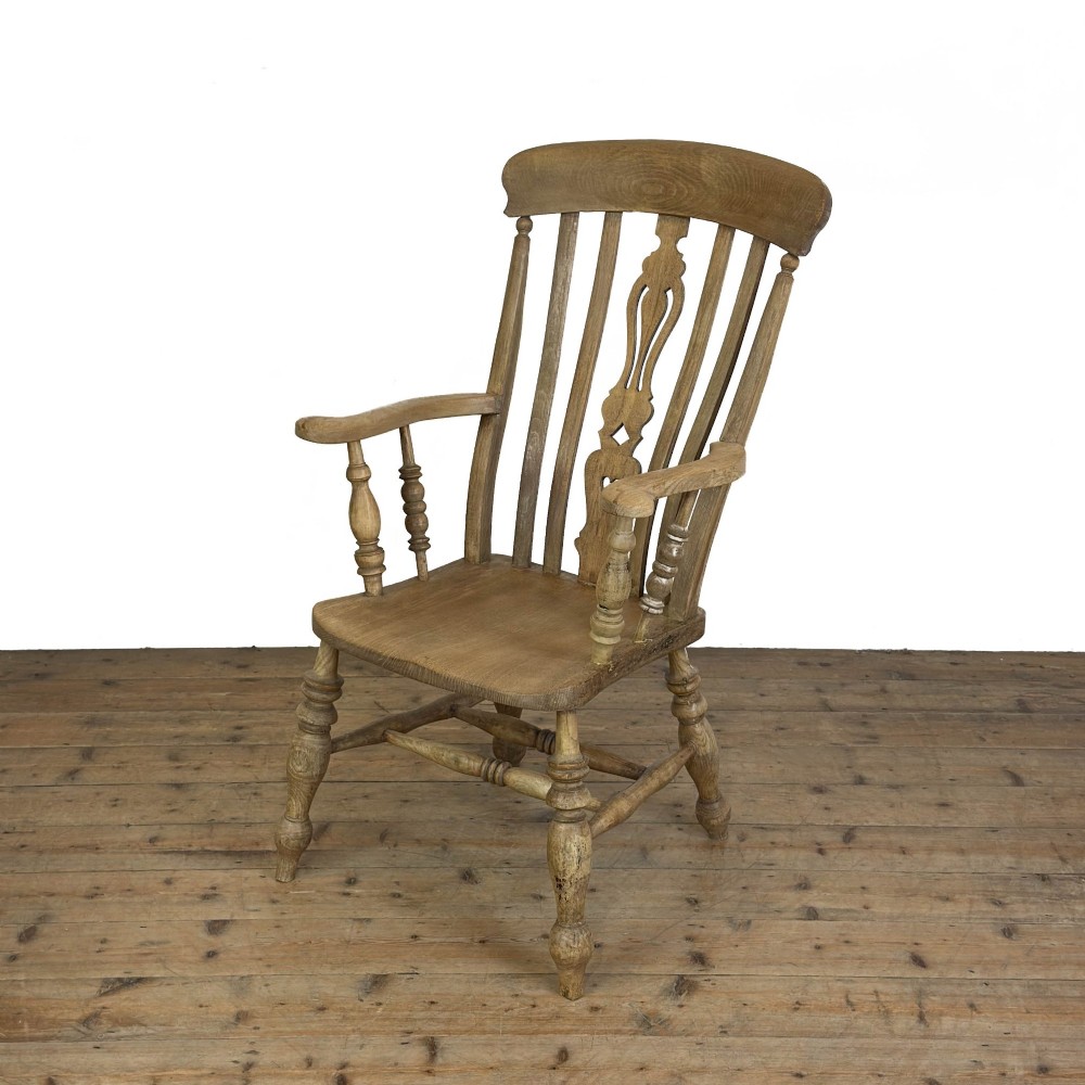 A traditional wooden Windsor armchair featuring a pierced back splat, turned arm supports, and a shaped saddle seat.