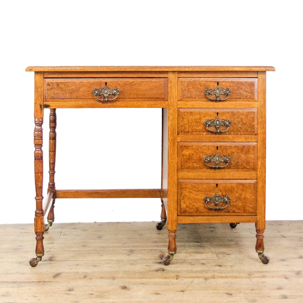 An antique Edwardian warm brown oak writing desk featuring five drawers with brass swing handles, turned legs, and brass castors.