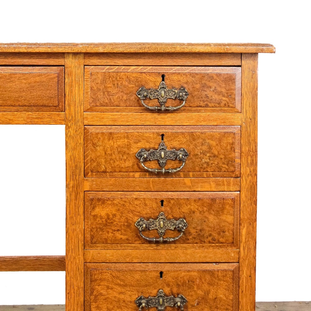 An antique Edwardian warm brown oak writing desk featuring five drawers with brass swing handles, turned legs, and brass castors. View II
