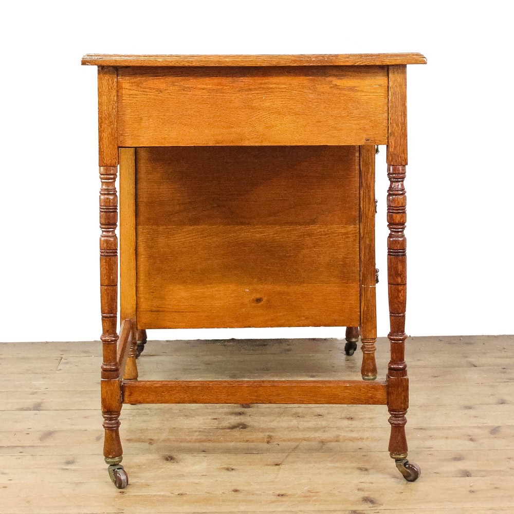 An antique Edwardian warm brown oak writing desk featuring five drawers with brass swing handles, turned legs, and brass castors. View III