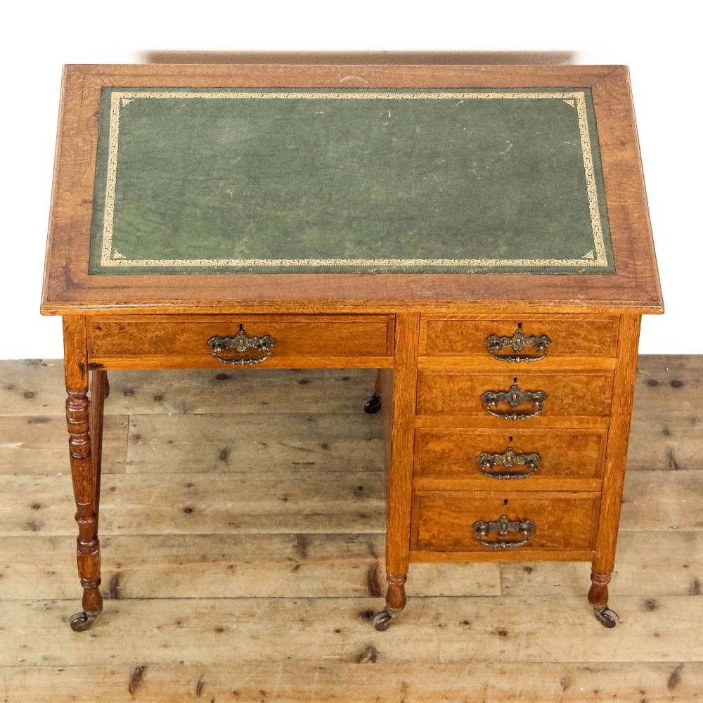 An antique Edwardian warm brown oak writing desk featuring five drawers with brass swing handles, turned legs, and brass castors. View V