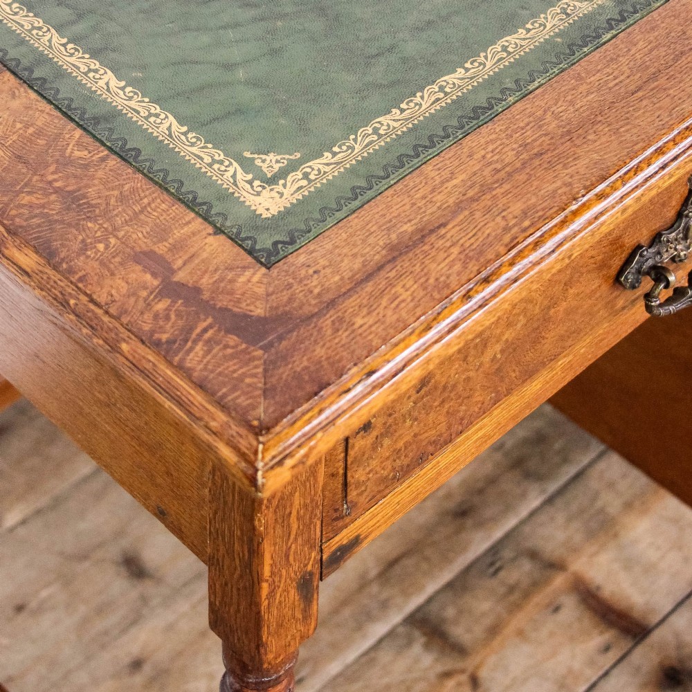 An antique Edwardian warm brown oak writing desk featuring five drawers with brass swing handles, turned legs, and brass castors. View VI