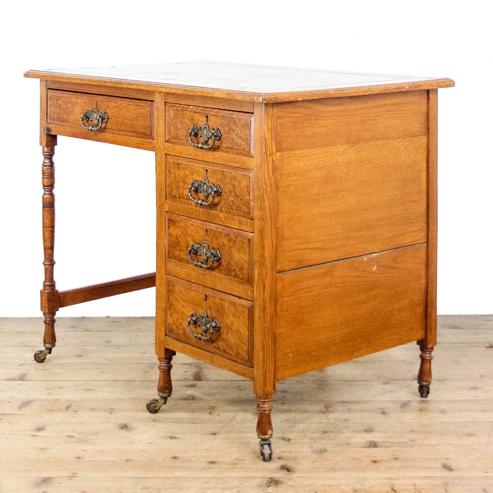An antique Edwardian warm brown oak writing desk featuring five drawers with brass swing handles, turned legs, and brass castors. View VII