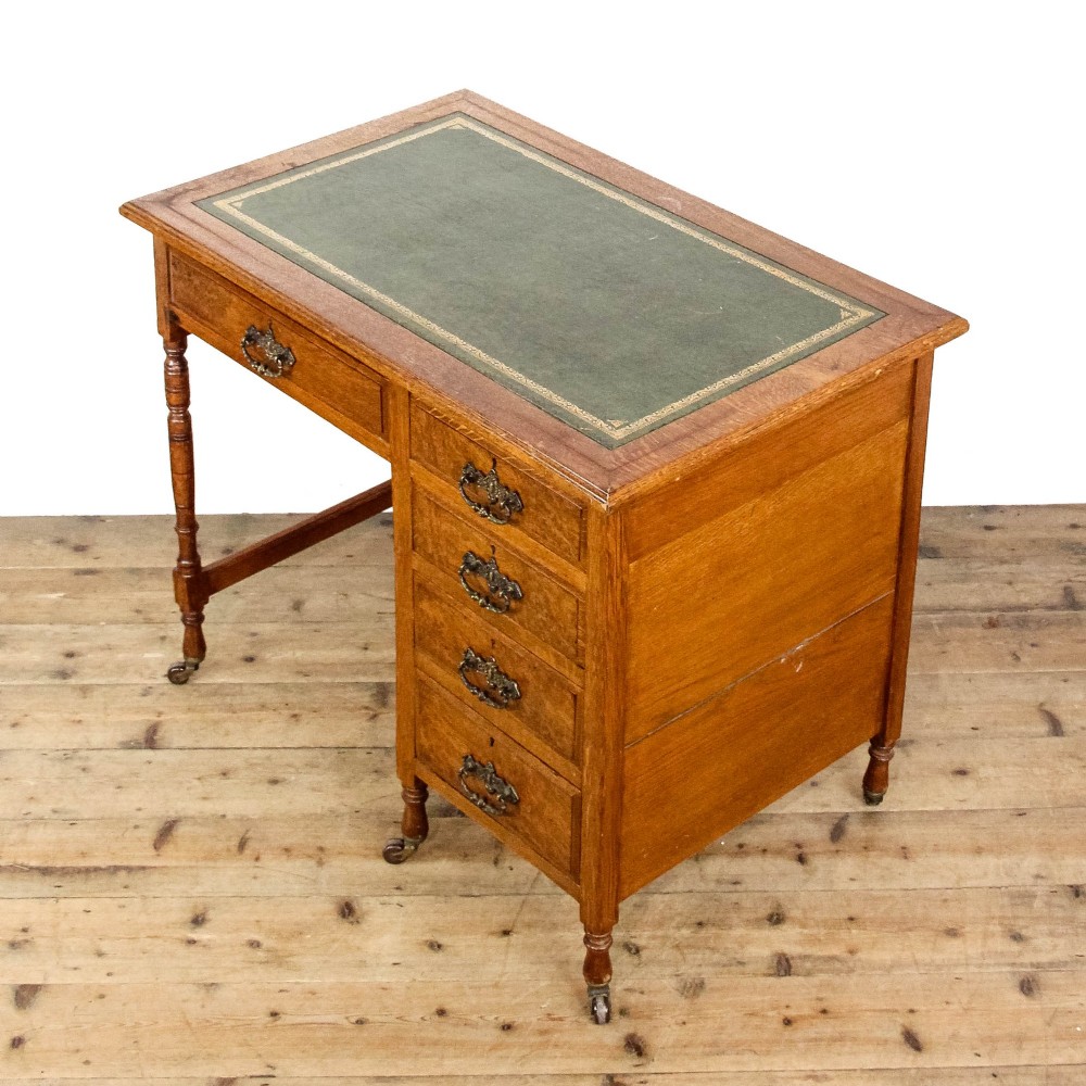 An antique Edwardian warm brown oak writing desk featuring five drawers with brass swing handles, turned legs, and brass castors. View VIII