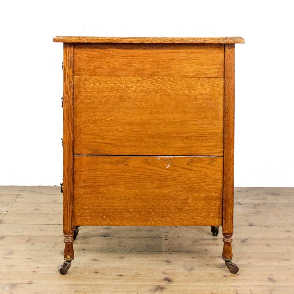 An antique Edwardian warm brown oak writing desk featuring five drawers with brass swing handles, turned legs, and brass castors. View IX