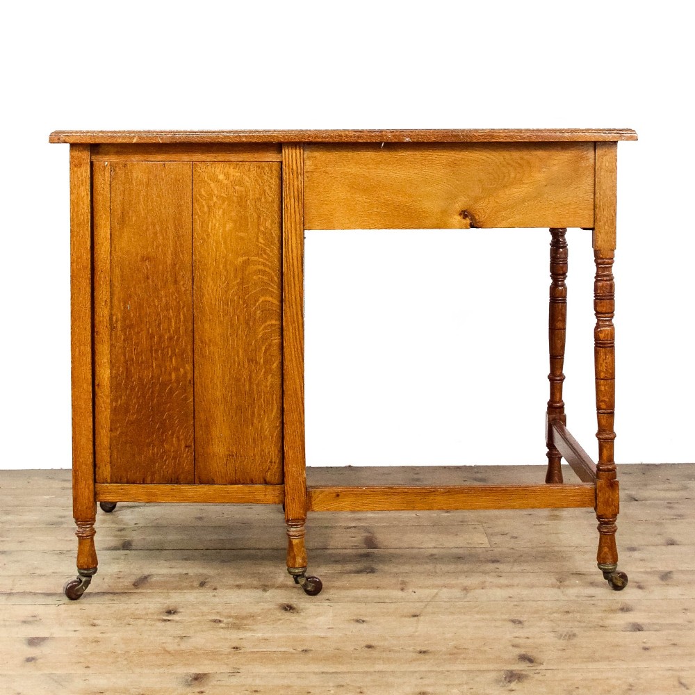 An antique Edwardian warm brown oak writing desk featuring five drawers with brass swing handles, turned legs, and brass castors. View X