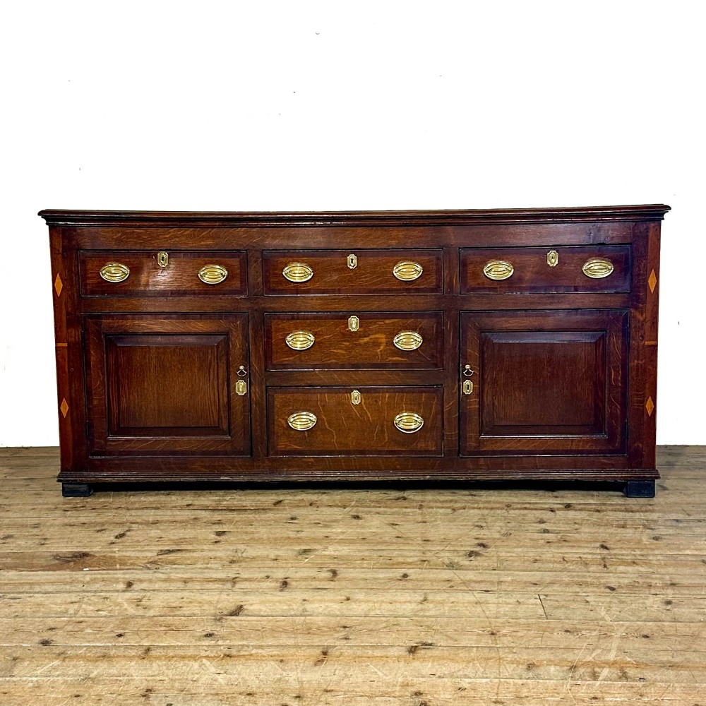 An antique Georgian oak dresser base featuring brass oval drop handles, panelled cupboard doors, central drawers, and geometric diamond inlay.