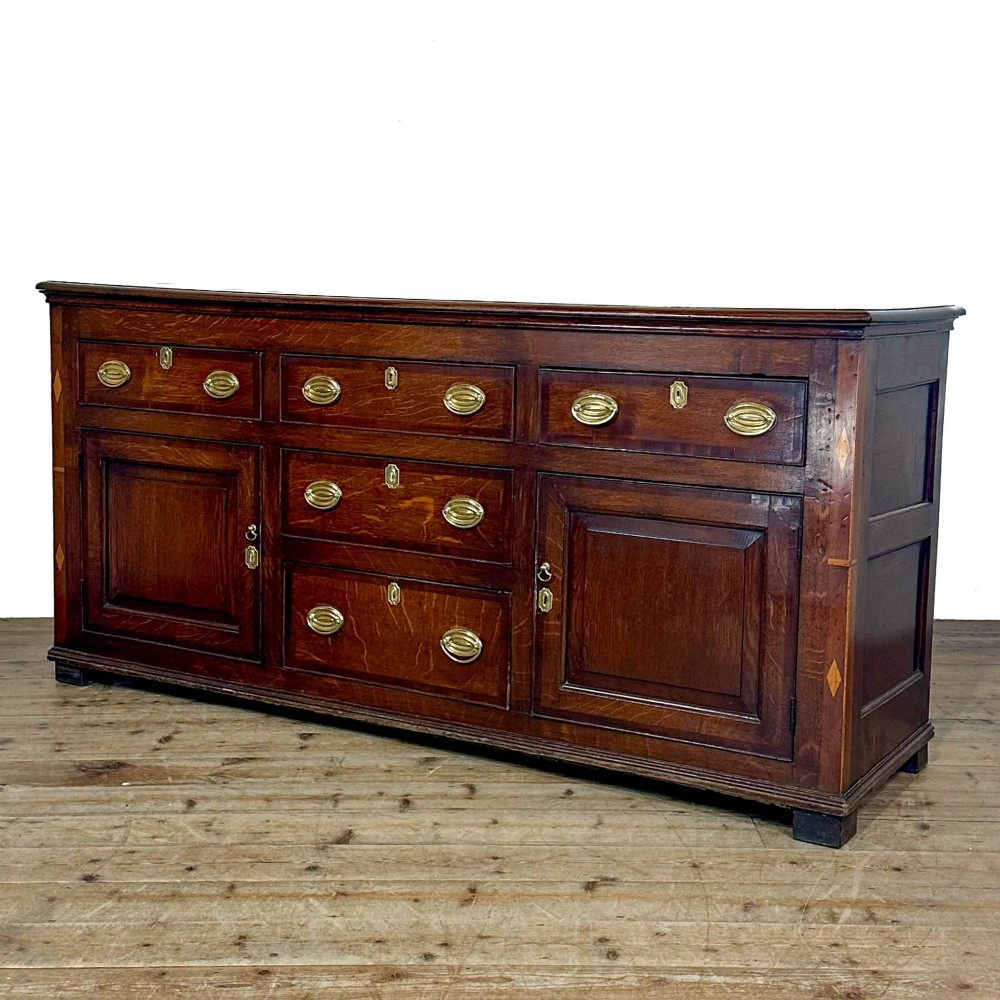 An antique Georgian oak dresser base featuring brass oval drop handles, panelled cupboard doors, central drawers, and geometric diamond inlay. View II