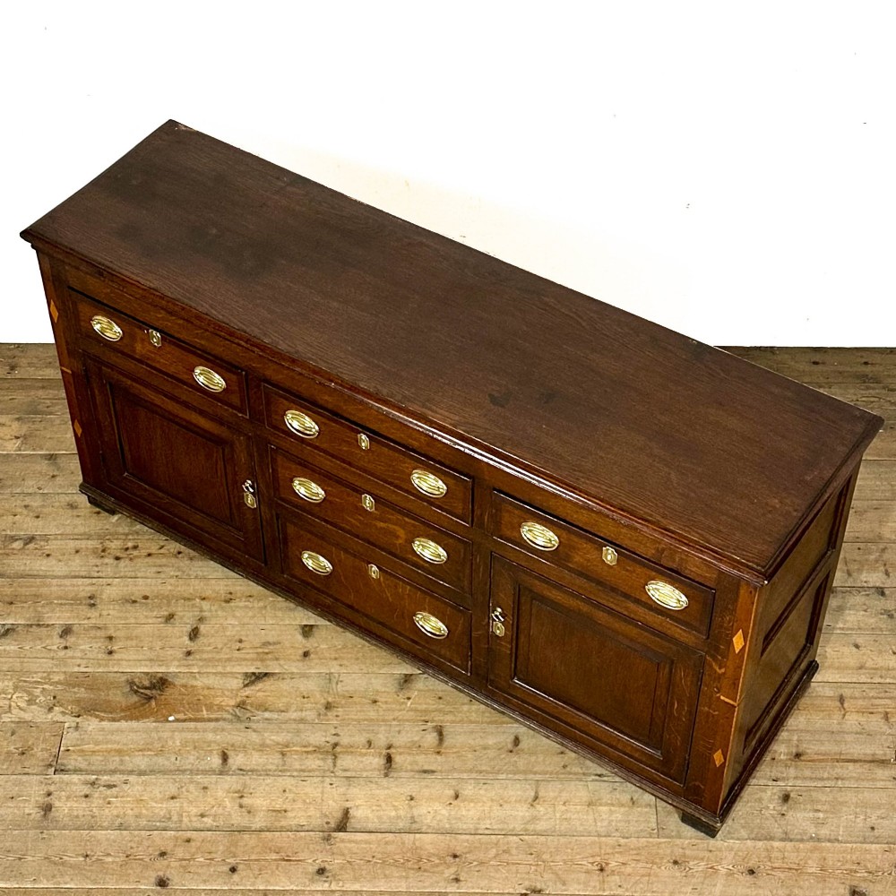An antique Georgian oak dresser base featuring brass oval drop handles, panelled cupboard doors, central drawers, and geometric diamond inlay. View III
